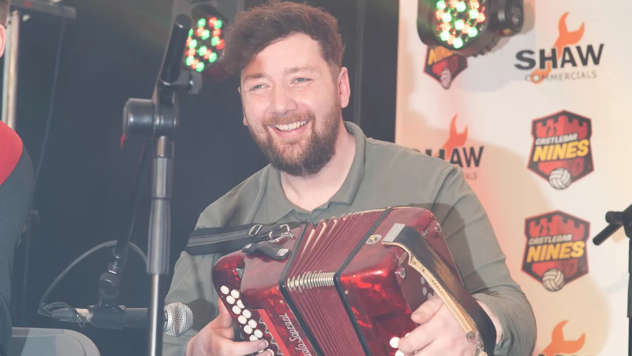 Accordion player smiling in front of the Castlebar 9s backdrop